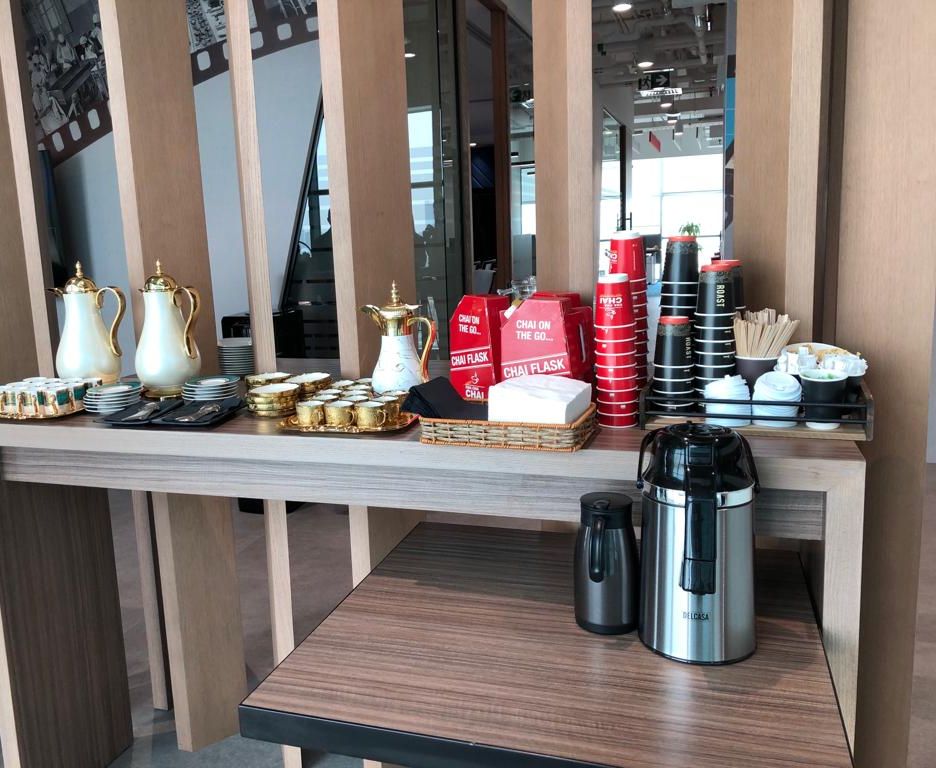 Hospitality table at an exhibition with gold gahwa dallahs, small cups, red Chai Flask boxes, stacked cups and two airpot flasks
